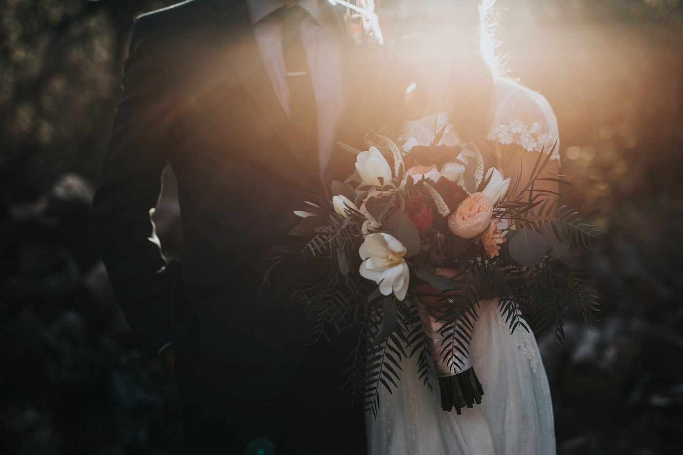 Bride holding a bouquet beside the groom in warm backlight