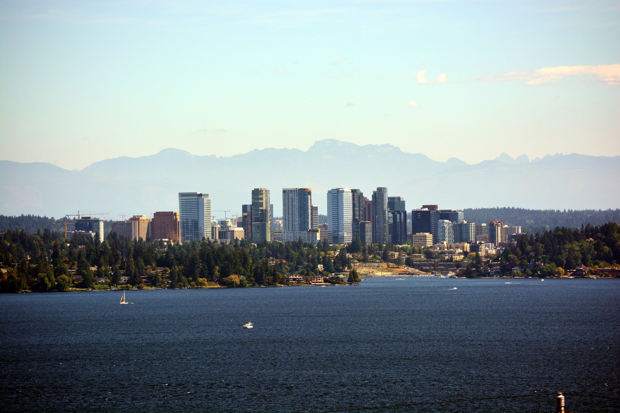Downtown Bellevue high-rises above a wooded Lake Washington shoreline with hazy Cascade peaks behind