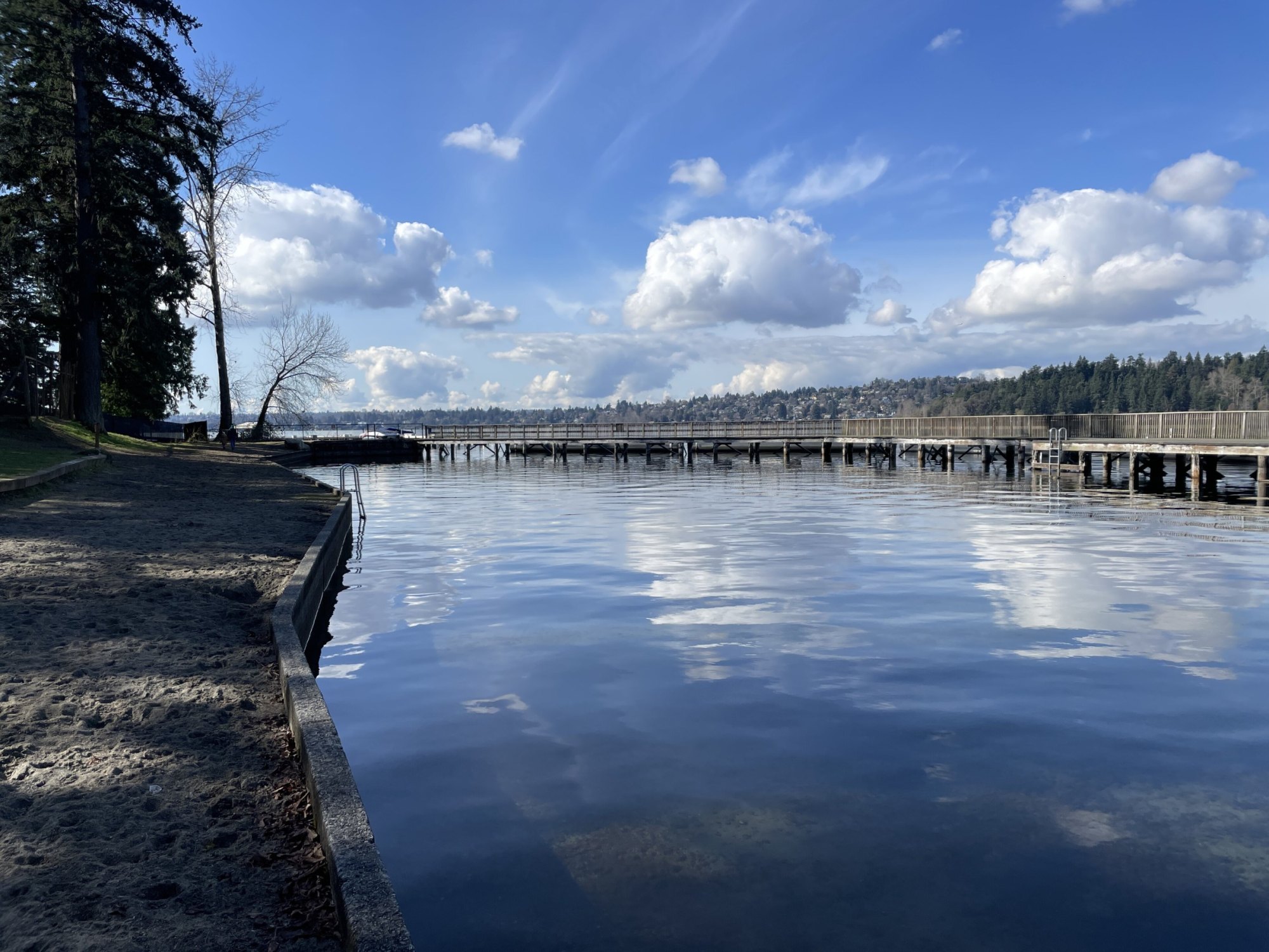 Calm Lake Washington reflecting white clouds beside a wooden pier and sandy Groveland Beach shoreline