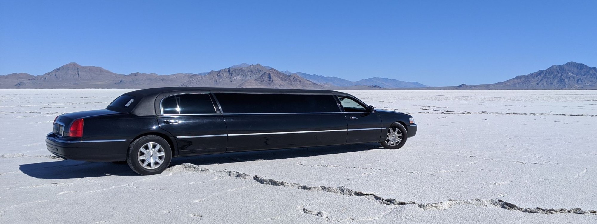 Black stretch limousine parked on white salt flats beneath a clear blue sky