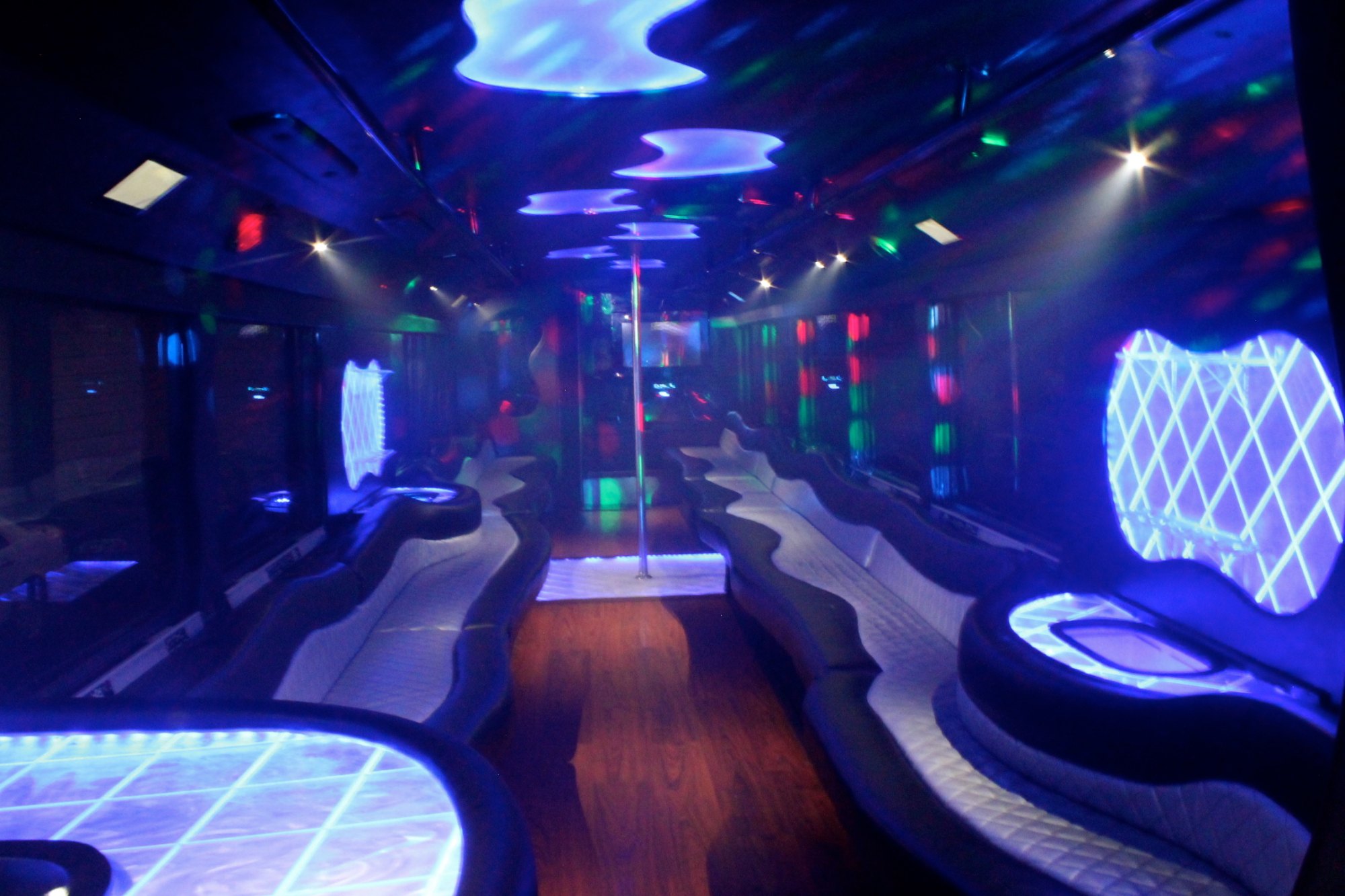 Party bus interior with long wraparound leather benches, wood floor and blue LED lighting