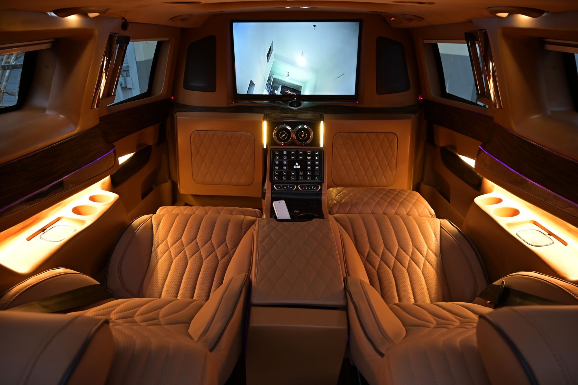 Executive van interior with quilted tan leather captain's chairs, warm ambient lighting and screen