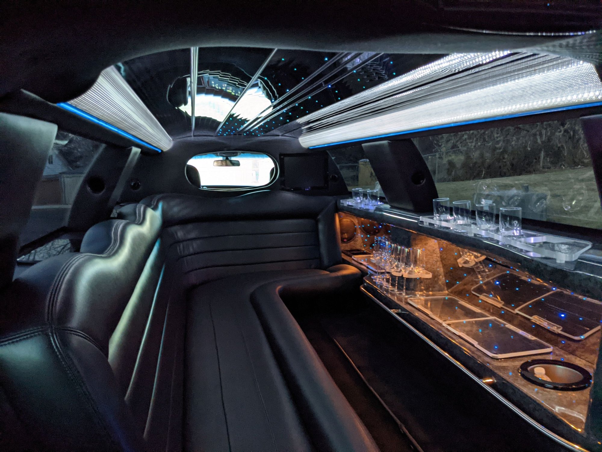 Limousine interior with black leather wraparound seating, lit glassware bar and starry LED ceiling
