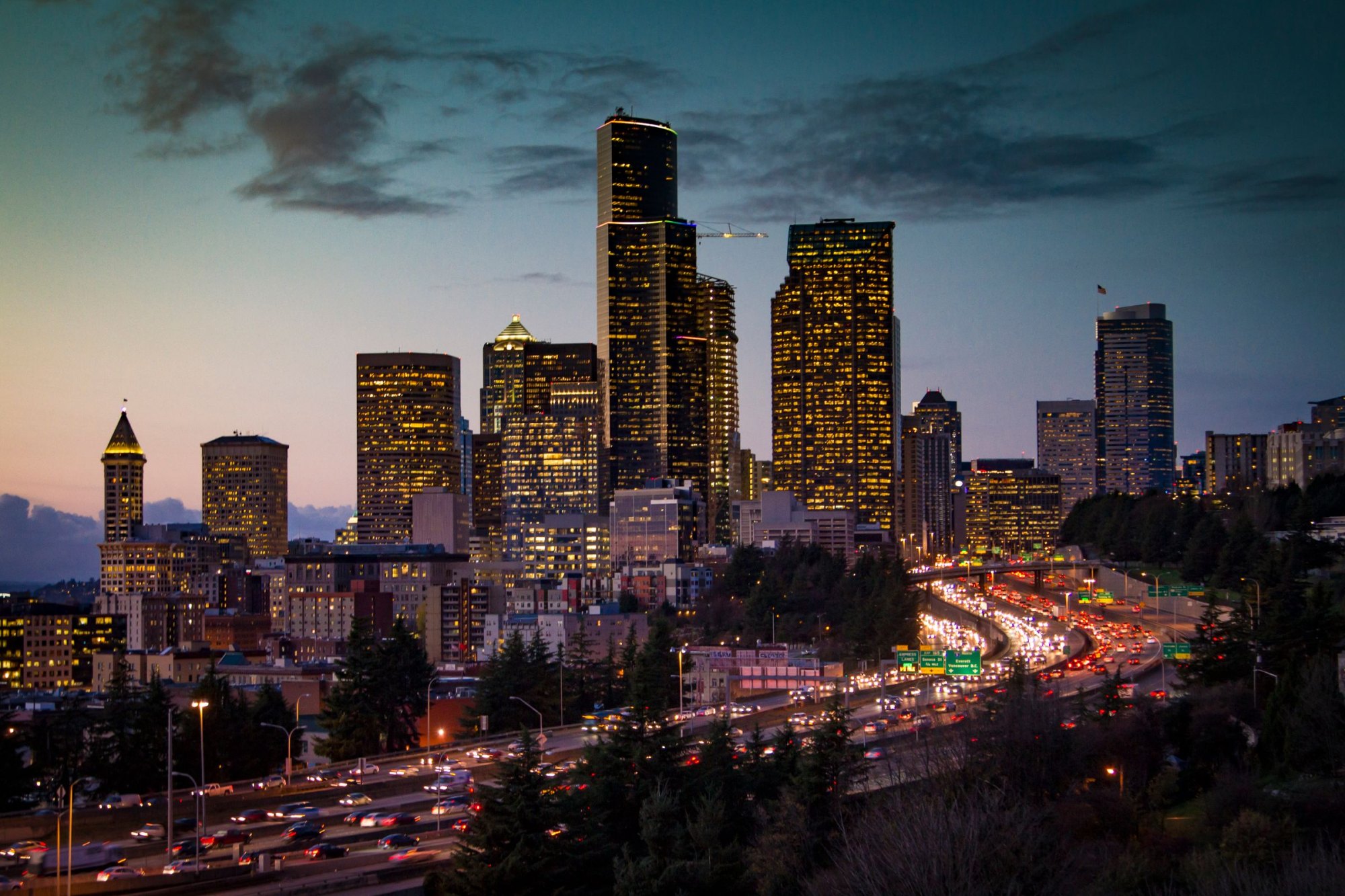 Seattle skyline glowing at twilight above a freeway filled with car light trails